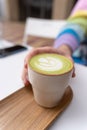Man Hands Holding Macha Latte Cup with Wooden Plate in Caffe