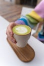 Man Hands Holding Macha Latte Cup with Wooden Plate in Caffe