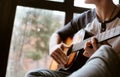 Man hands sitting on the big window windowsil and playing on guitar - fingers close up image Royalty Free Stock Photo