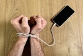 Man hands wrapped on wrists with mobile phone cable handcuffed in smart phone networking addiction concept Royalty Free Stock Photo