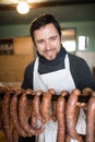 Man hanging homemade raw sausages on wooden stick.