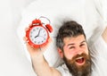 Man with happy face lies on pillow, holds alarm clock.