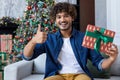 Man happy and smiling looking at camera sitting on sofa in living room, holding gift for New Year and Christmas holidays Royalty Free Stock Photo