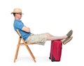Man in a hat, shorts and a T-shirt, asleep sitting on a chair in anticipation, with his legs on a red suitcase. Isolated on white Royalty Free Stock Photo