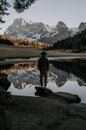 A man with a hat is standing by a mountain lake in the Dolomites. The mountains and the rest of the landscape are reflected in the Royalty Free Stock Photo