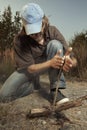 Man camping in nature making fire with wood stick friction by hands