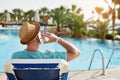 Man in hat using mobile phone on vacation by the pool in hotel, concept of a freelancer working for himself on vacation Royalty Free Stock Photo