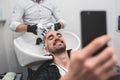 Man having his hair washed in hairdressing salon and using phone Royalty Free Stock Photo
