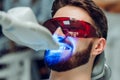 Man having teeth whitening by dental UV whitening device,dental assistant taking care of patient,eyes protected with glasses. Royalty Free Stock Photo