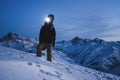 Man with headlamp and backpack wearing ski wear standing in front of amazing winter mountain view. Traveler climb at night on the Royalty Free Stock Photo