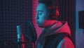 A man in headphones rapping through the pop-filter in the microphone - studio in neon lighting