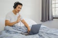 Man with headphones sitting in bed and waving hand having video call on laptop. Royalty Free Stock Photo