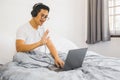 Man with headphones sitting in bed and waving hand having video call on laptop coronavirus quarantine. Royalty Free Stock Photo