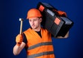 Man in helmet, hard hat carries toolbox and holds hammer, blue background. Handyman concept. Worker, repairer, repairman Royalty Free Stock Photo