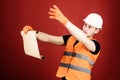 Man in helmet, hard hat holds building plan, controls works, red background. Architect concept. Engineer, architect Royalty Free Stock Photo