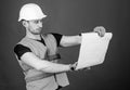 Man in helmet, hard hat holds building plan, controls works, red background. Engineer, architect, builder on strict face Royalty Free Stock Photo