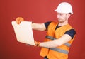 Man in helmet, hard hat holds building plan, controls works, red background. Engineer, architect, builder on strict face Royalty Free Stock Photo