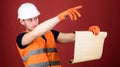 Man in helmet, hard hat holds building plan, controls works, red background. Foreman concept. Engineer, architect Royalty Free Stock Photo