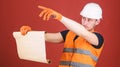 Man in helmet, hard hat holds building plan, controls works, red background. Foreman concept. Engineer, architect Royalty Free Stock Photo