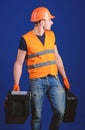 Man in helmet, hard hat holds toolbox and suitcase with tools, blue background. Equipped repairman concept. Worker Royalty Free Stock Photo