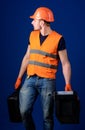 Man in helmet, hard hat holds toolbox and suitcase with tools, blue background. Equipped repairman concept. Worker Royalty Free Stock Photo