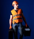 Man in helmet, hard hat holds toolbox and suitcase with tools, blue background. Professional repairman concept. Worker Royalty Free Stock Photo