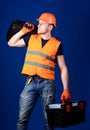Man in helmet, hard hat holds toolbox and suitcase with tools, blue background. Worker, handyman, repairman, builder on Royalty Free Stock Photo
