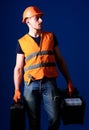 Man in helmet, hard hat holds toolbox and suitcase with tools, blue background. Worker, handyman, repairman, builder on Royalty Free Stock Photo