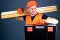 Man in helmet, hard hat holds toolbox and wooden beams, grey background. Professional woodworker concept. Carpenter