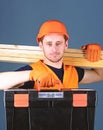 Man in helmet, hard hat holds toolbox and wooden beams, grey background. Professional woodworker concept. Carpenter