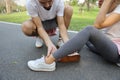 Man helping jogger woman who hurt the ankle from too much exercise in the park Royalty Free Stock Photo