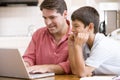 Man helping young boy in kitchen with laptop Royalty Free Stock Photo