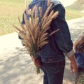 The man hides the grass flowers behind his back to surprise his girlfriend