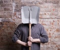 A man hides his face behind a shovel.