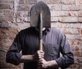 A man hides his face behind a shovel.