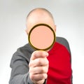 man hides his face with a magnifying glass. The concept of searching for a person in a database. Look at the world incognito.
