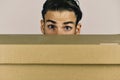 Man hiding behind cardboard box on grey background