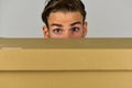 Man hiding behind cardboard box on grey background
