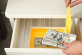 Man hiding dollar banknotes in cabinet indoors. Money savings