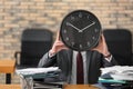 Man hiding face behind clock at table in office. Time management concept Royalty Free Stock Photo