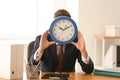 Man hiding face behind clock at table in office. Time management concept Royalty Free Stock Photo