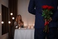Man hiding roses for his beloved woman in restaurant at romantic dinner