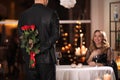 Man hiding roses for his beloved woman in restaurant at Valentine`s day dinner