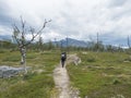 Man hiker with backpack walking at footpath in Lapland landscape with snow capped mountain, birch tree and green bush at