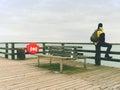 Man hiker with backpack on wet mole above sea. Misty morning with smooth water