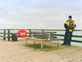 Man hiker with backpack on wet mole above sea. Misty morning with smooth water