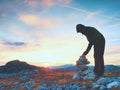 Man hiker is building pebbles pyramid. Stones on Alps mountain summit. Daybreak horizon Royalty Free Stock Photo