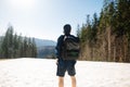 Man hiker in casual clothes and a cap with a backpack on his back stands on a snowy mountain and looks ahead, view of the back Royalty Free Stock Photo