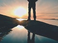 Man hiker legs in high boots mirrored in water pool, sea with sunset sun. Tourist figure on rocky Royalty Free Stock Photo