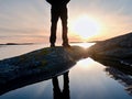 Man hiker legs in high boots mirrored in water pool, sea with sunset sun. Tourist figure on rocky Royalty Free Stock Photo